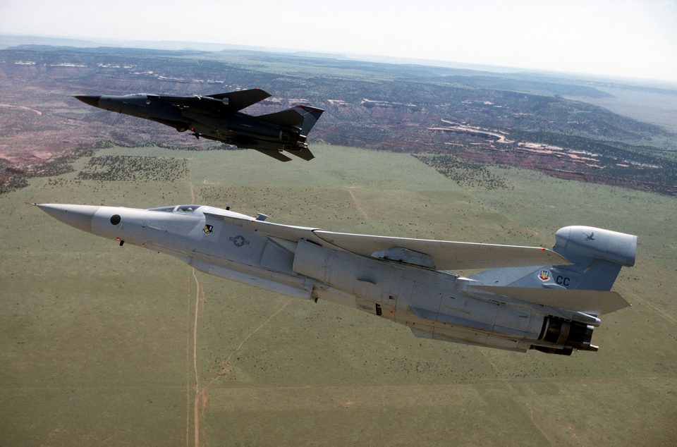 A low-altitude aerial view of an EF-111A Raven (foreground) and an F-111F .The aircraft belong to the 27th Fighter Wing, which transitioned from the F-111Ds to F-111Fs and added EF-111As.