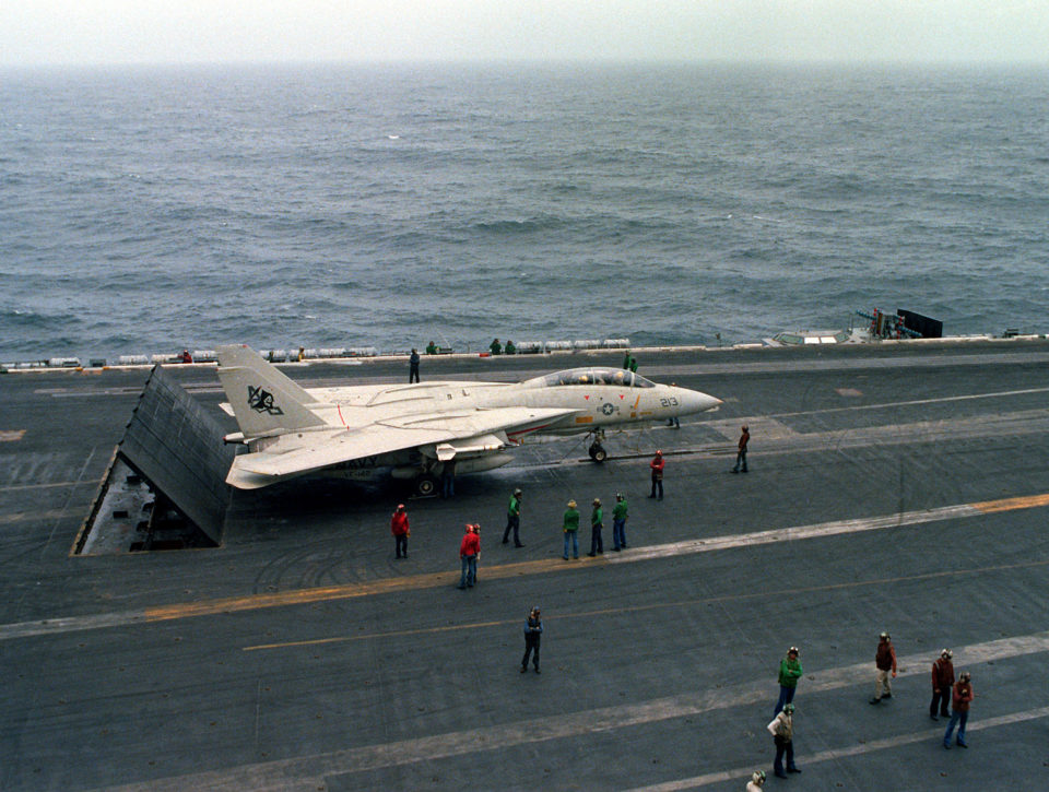 An elevated left side view of an F-14 Tomcat aircraft being prepared for a catapult-assisted takeoff from the flight deck of the nuclear-powered aircraft carrier USS DWIGHT D. EISENHOWER (CVN-69). The F-14 is assigned to Fighter Squadron 142 (VF-142). Three blast deflector panels are raised at the rear of the aircraft.