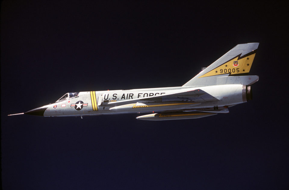 An air-to-air left side view of an F-106 Delta Dart aircraft being piloted by a squadron commander during a training mission. The aircraft are from the 5th Fighter Interceptor Squadron.