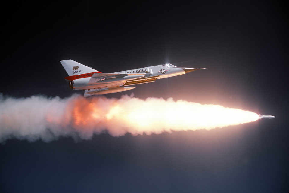 An air-to-air right side view of an F-106 Delta Dart aircraft after firing an ATR-2A missile over a range. An auxiliary fuel tank is on each wing. The aircraft is assigned to the 194th Fighter Interceptor Squadron, California Air National Guard.